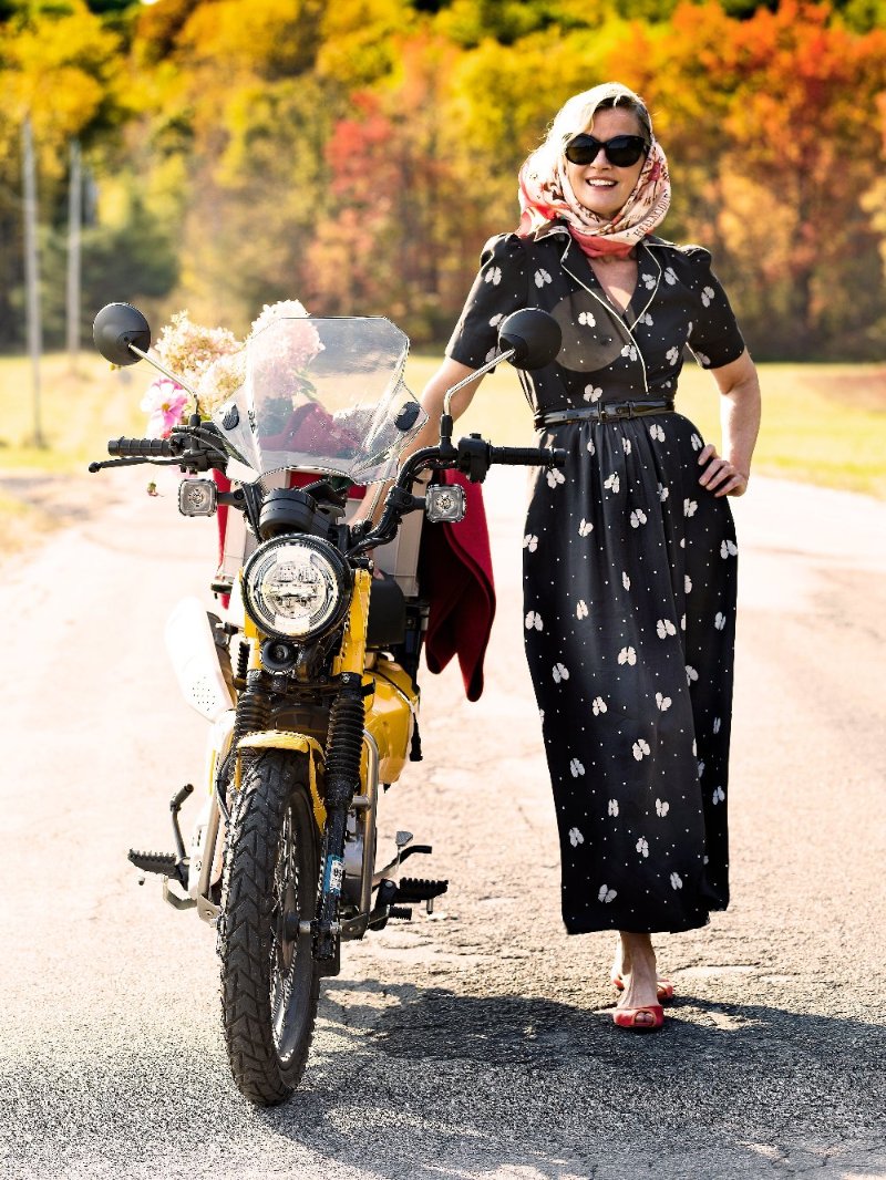 Gretchen wearing black wrap dress with white bows, holding a yellow scooter.