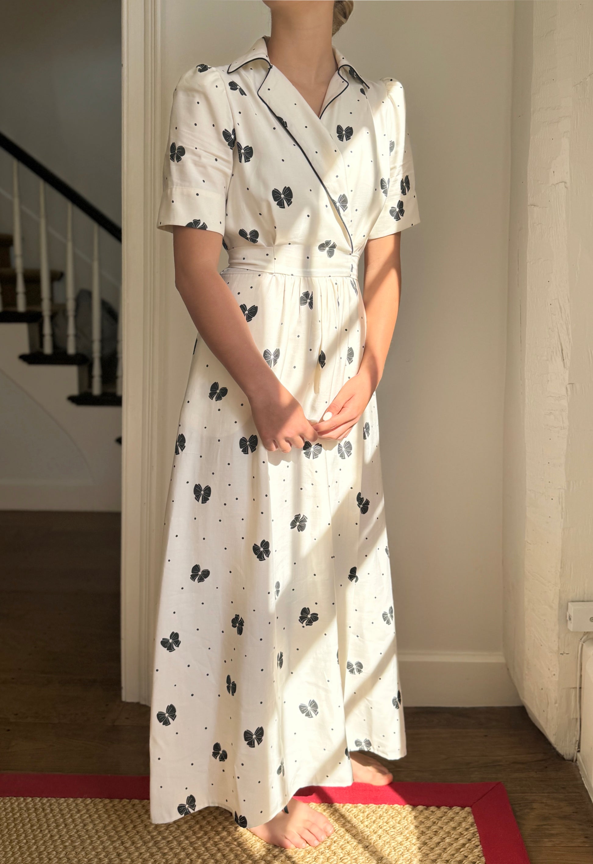 Full length shot of cream wrap dress with black bows.